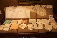 Wide view of large assortment of vintage table linens arranged on a couch, including serviettes and a small table cloth.