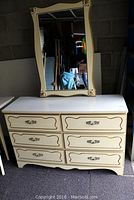 Front view of the cream-colored dresser with all six drawers visible and matching mirror resting on top.