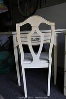 Rear view of cream-colored chair with shield back and curved top rail next to vanity.