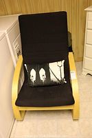 Front view of the IKEA Poang chair with black fabric upholstery and light wood bentwood frame, showing included decorative cushion.