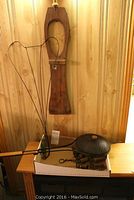 Wire rug beater with heart-shaped wire frame, long wooden boot jack on a wooden surface against wood panel wall