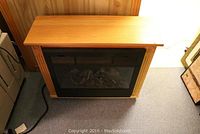 Full front view of the electric fireplace showing the wood frame and black vent panel with faux log display inside.