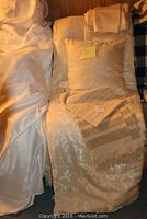 Full view of the cream damask queen comforter, shams, a cushion, and a striped throw blanket arranged on a bed.