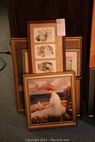 Five framed art pieces stacked showing variety of vintage portrait prints and one large framed painting of woman reading by the sea