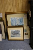 Two framed prints leaning against wall, images show countryside barn and horses scenes by Peter Etril Snyder with cream mats and gold frames
