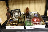 Overview of two boxes containing various collectibles including clocks, glassware, and metal items