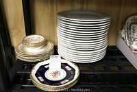 Stack of white dinner plates with decorated edges next to arranged dessert and fruit napkin plates with floral and gold detail.