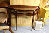 Full front view of the dark stained hall table placed against a paneled wall, showing tapered legs and metal tipped feet.