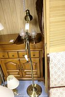 Brass floor lamp shown with adjustable arm, round weighted base and brass lampshade, pull chain switch visible.