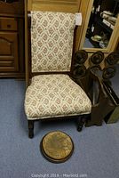 Armless wood framed chair with floral upholstery and round footstool placed on floor