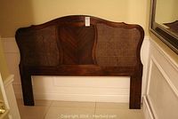 Front view of the complete wood framed headboard with cane inserts, showing overall design and size next to a wall.