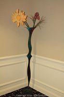 Full view of the green metal vase statue with yellow and red faux flowers inside, showing the shape and height.