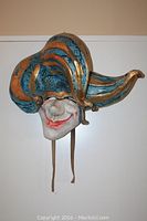 Front view of paper mache jester mask showing colorful jester hat with gold and blue stripes, smiling white face with red lips.