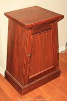 Front view of wooden cabinet showing trapezoidal shape, paneled door, and metal knob.