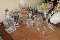 All crystal and glass items displayed on cardboard surface including a Waterford ice bucket, two decanters with stoppers, a striped glass pitcher, a crystal vase, and an aerating decanter.