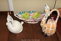 Lot display with the white ceramic piggy bank, colorful serving dish with pears, and giraffe teapot