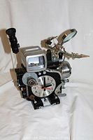 Full view of the clock camera art sculpture showing the front and left side with magnifying glass and viewfinder attachments.