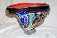 Side view of colorful handmade art glass bowl showing swirling colors with clear glass ruffle accents and orange interior.