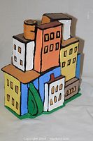 Front and side view of the 3D mixed media sculpture showing colorful building shapes and painted details.