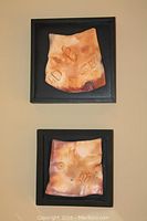 Two stoneware art pieces measuring 9x9 inches mounted in black shadow box frames, showing textured abstract artisan patterns in warm earth tones.
