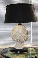 Full view of one lamp on a table showing ceramic pine cone base and black shade.