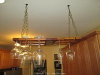 Wooden hanging wine rack suspended by metal chains with various types of wine glasses hanging upside down.