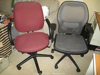 Pair of office chairs side by side on carpeted floor, red fabric chair and black mesh chair