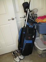 Photo showing golf bag with assorted golf clubs, beige golf shoes size 12W next to it, and some surrounding storage bins.
