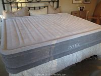 Light grey Intex inflatable mattress fully inflated on bed frame, with vertical air chambers and white top surface.