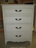 Front view of ivory finish wooden dresser showing four drawers with decorative handles and scalloped bottom edge.