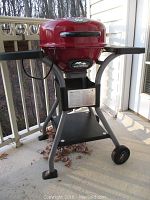 Full view of the red Masterbuilt electric grill mounted on a grey frame with wheels, placed on a porch.
