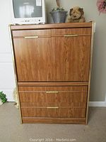 Front view of laminate chest of drawers showing wood grain finish, brass handles, some wear, and flip-down compartment on top.