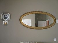 Wall photo showing oval ornate mirror and octagonal clock side by side mounted on beige wall