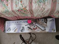 Photo showing full box of Simplex Plus 40" Capacity Mat Cutter Model 750 resting on a floor with floral furniture in the background.