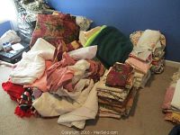 Wide view showing large collection of various linens and comforters piled on the floor