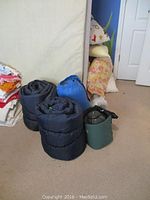 Three rolled sleeping bags, two black and one blue, with camping lights visible nearby.
