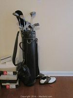 Black Brunswick golf bag standing upright with multiple assorted golf clubs inserted. Bag shows wear around edges and strap. Several golf club heads visible with metal shafts.