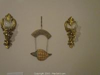 Pair of gilded wall sconces mounted on the wall, flanking a sea shell Welcome sign suspended by wire.