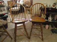 Front view of two wooden pub height spindle chairs with natural finish, spindle backs, contoured seats, and turned legs.