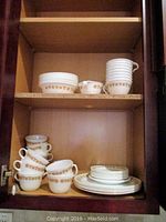 Shelf with stacked Corelle unusual dishware including cups, mugs, plates, and bowls with gold decorative rim.