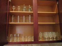 Straight on view of two cabinet shelves showing several types of glasses including tall classic glasses on second shelf, short classic glasses and cut glass glasses on bottom shelf
