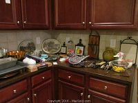 Wide view of corner kitchen counter showing baking pans, decorative plates, grilling planks, knives, and various kitchen tools and decor items