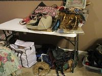 Large collection of purses, duffels, and tote bags arranged on tables and floor with varying patterns and colors.