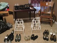 Wide view of women's shoes arranged on floor around two small white metal shoe racks with decorative bulb design.