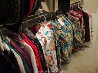 Wide view of multiple women's tops hanging in a closet rack showing variety of colors and patterns.