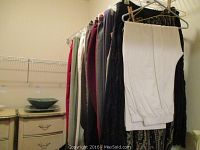 Clothing rack with approximately 12 pairs of women's pants in various colors including white, black, red, grey, and patterned.
