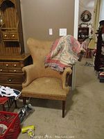 Front view of large upholstered high back armchair with a folded patterned blanket draped over one armrest.