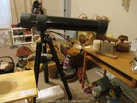 Full view of black Tasco telescope mounted on adjustable tripod, positioned indoors among other household items.