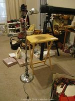 Photo of a single wooden TV table and a chrome floor lamp on carpet, showing wear on table top and curved lamp arm with dome-shaped shade.