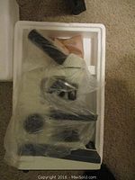 View of microscope wrapped in plastic inside styrofoam packaging showing eyepiece and base.